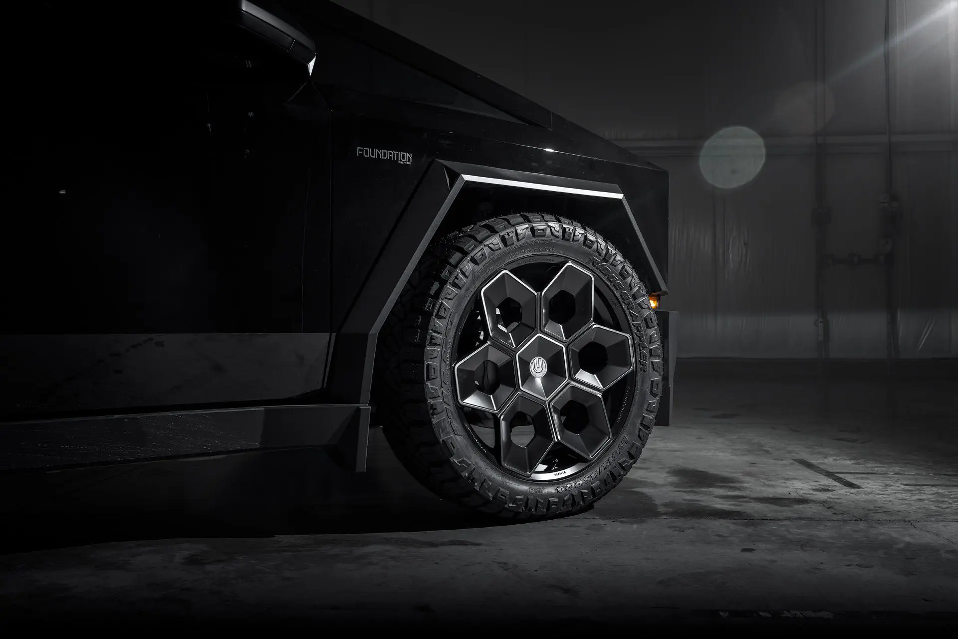 Side view of Tesla Cybertruck equipped with Unplugged Performance 24-inch Cybrhex Wheels in Satin Black, captured in a high-contrast lighting setup to emphasize the truck's angular body and robust wheels.